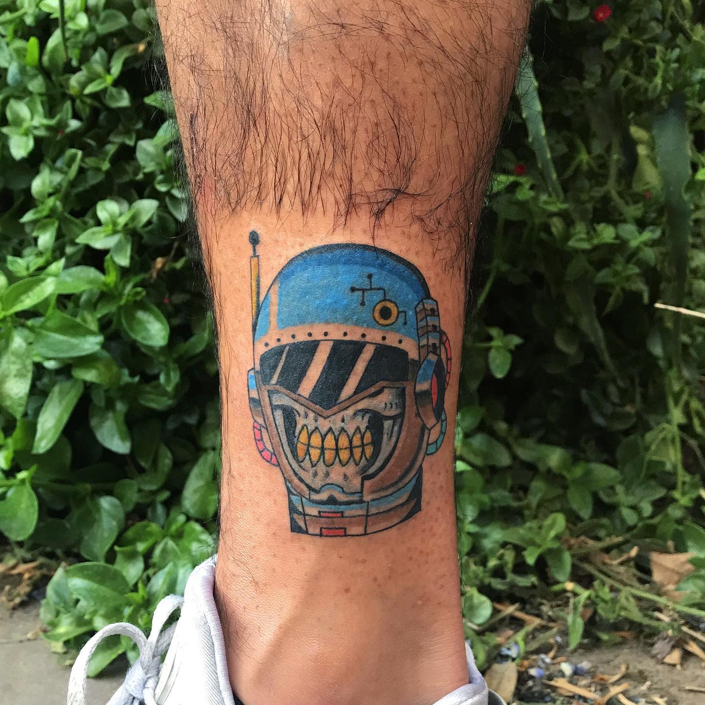 Colorful cyberpunk tattoo on lower leg featuring a stylized robotic skull with a blue helmet and yellow teeth